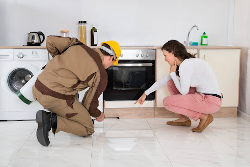 pest control technician and home owner looking under a stove 